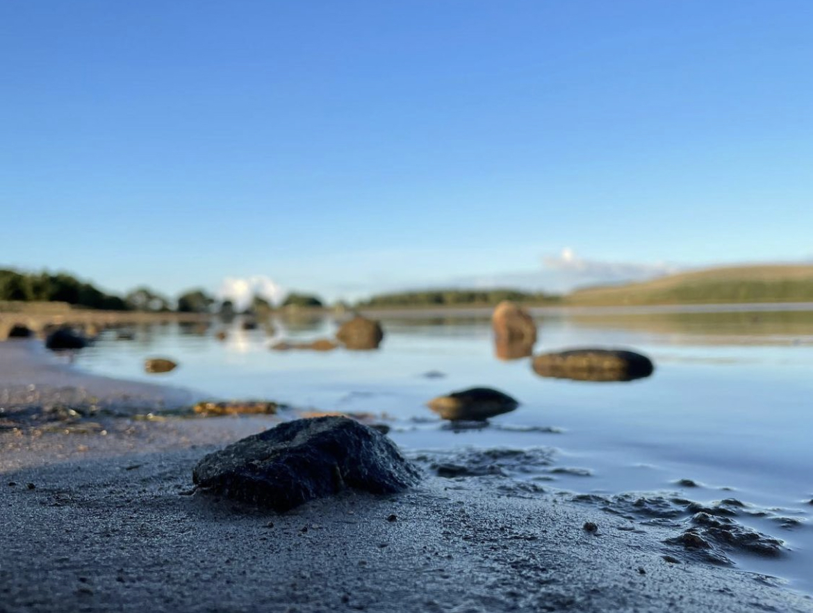 Ground level photo of a beach with blue skies and still waters.